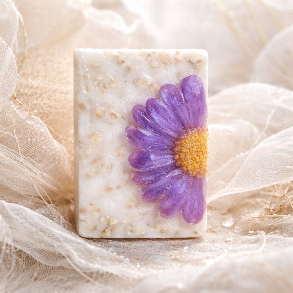 Square soap bar with a purple flower embedded on a soft fabric background