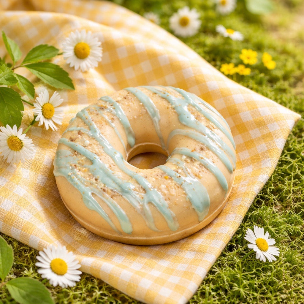 Donut soap with light blue glaze on a yellow checkered cloth with daisies in a natural setting