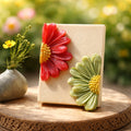 Decorative soap with red and green floral designs on a wooden surface with blurred flowers in the background.
